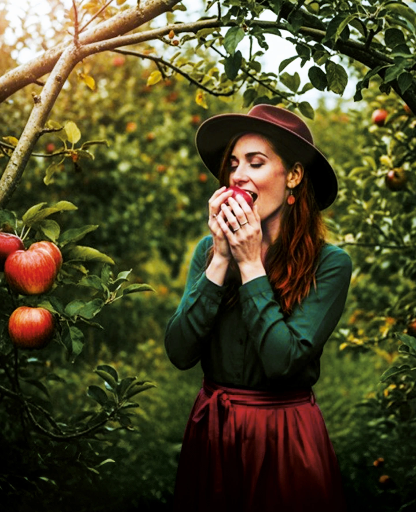 Woman in an apple orchard happily putting an apple to her mouth.